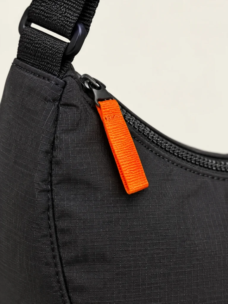 Close-up of Signal zip pull tab on Half-Moon Zip Bag curved top zip